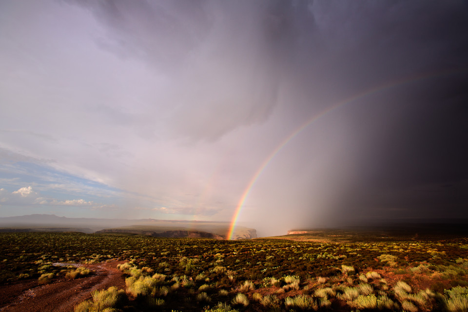 A powerful thunderstorm that dropped heavy rain and pea-sized hail moves off over Dead Indian Canyon along the Little Colorado River. This canyon eventually connects to the Grand Canyon. As the storm departs, water runs through the desert and a stunning rainbow seems to disappear into the canyon itself.