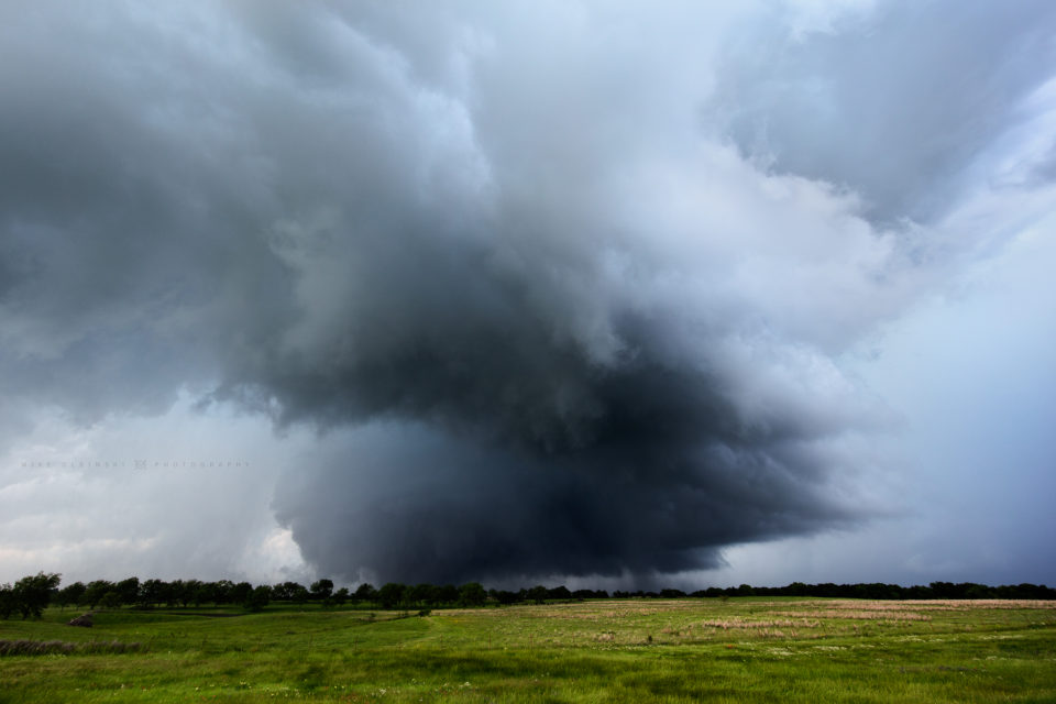 A mile-wide wedge tornado hangs out in the dark area beyond the trees as it slowly moves towards the town of Sulphur, Oklahoma.