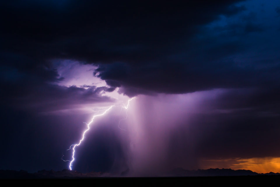 A long lightning strike acts like an off-camera flash to help illuminate an intense microburst over the Eagletail Mountains and Courthouse Rock.